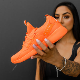 model wearing bracelet holds orange sneaker womens at angle