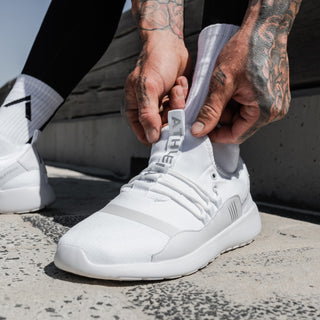 tattooed guy putting on his white casual sneakers